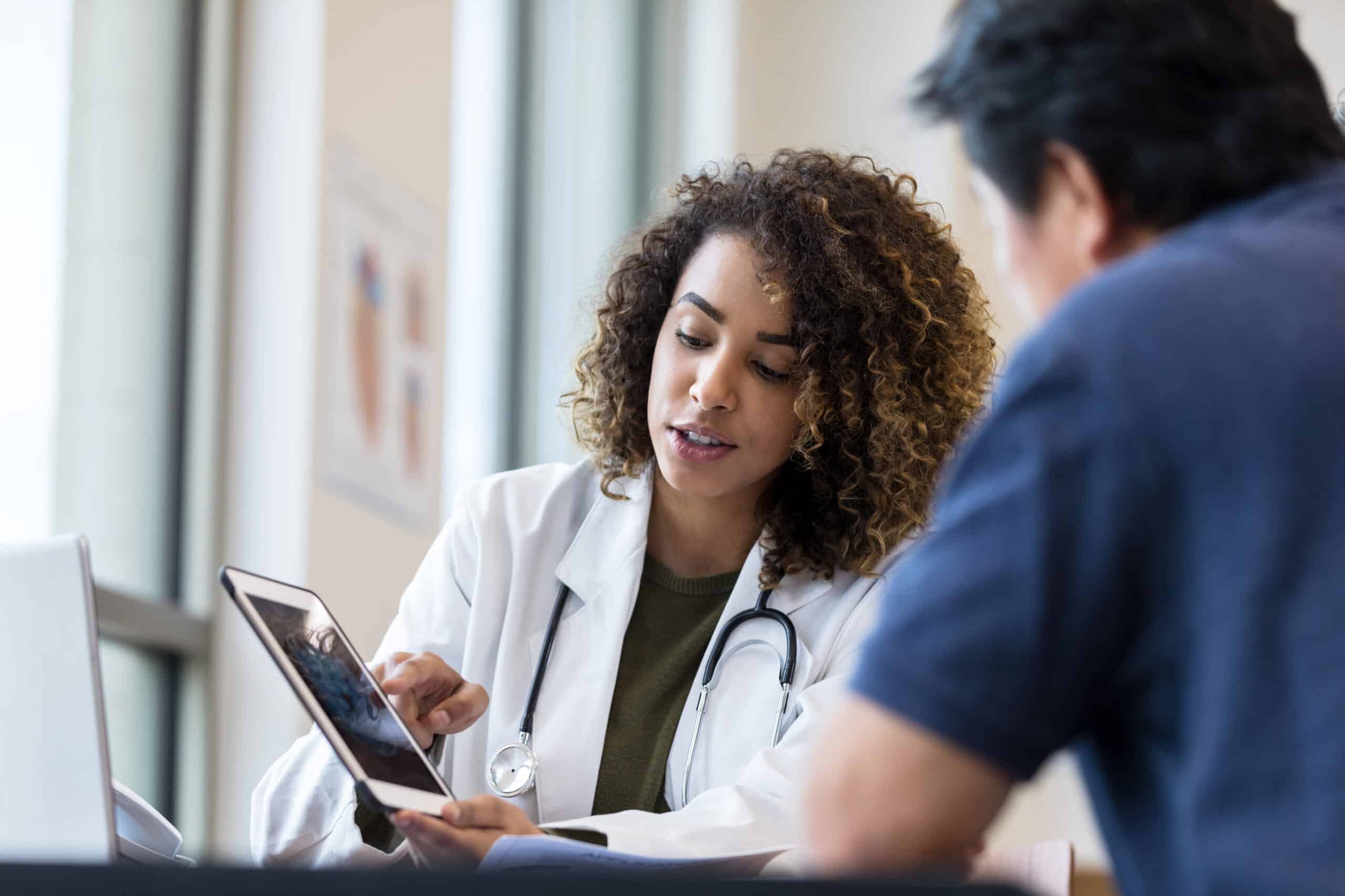 Female doctor uses tablet to show x-ray to senior man The mid adult female doctor uses the digital tablet to show the x-ray to the unrecognizable senior man.